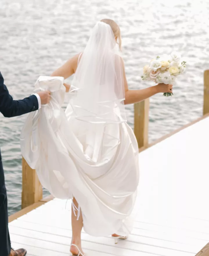 Grace and Lucas walk out on a dock of a lake in their wedding day attire