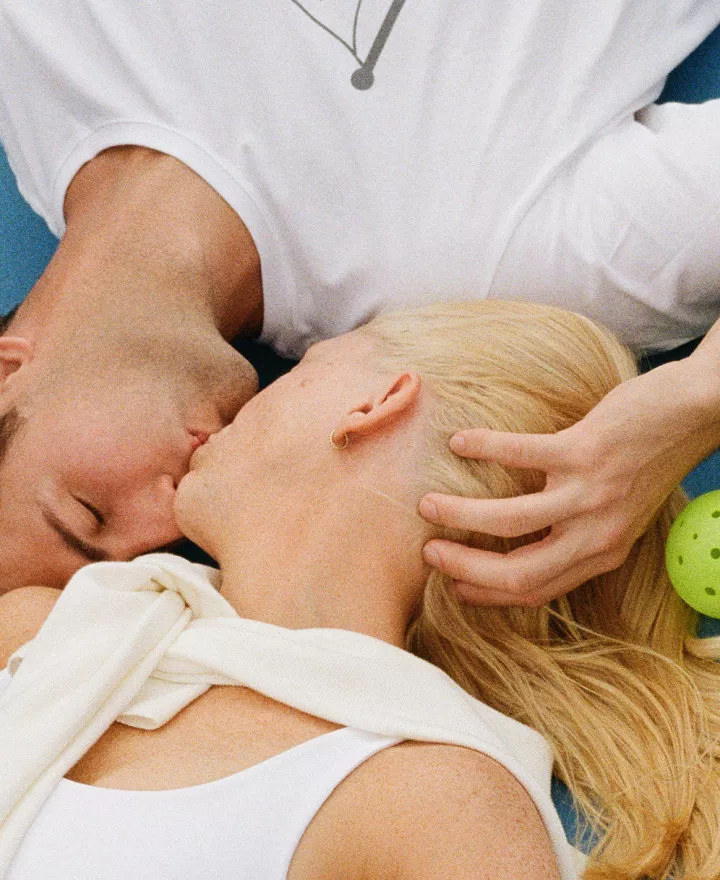 Jennifer and Sean lay on the pickleball court and share a kiss