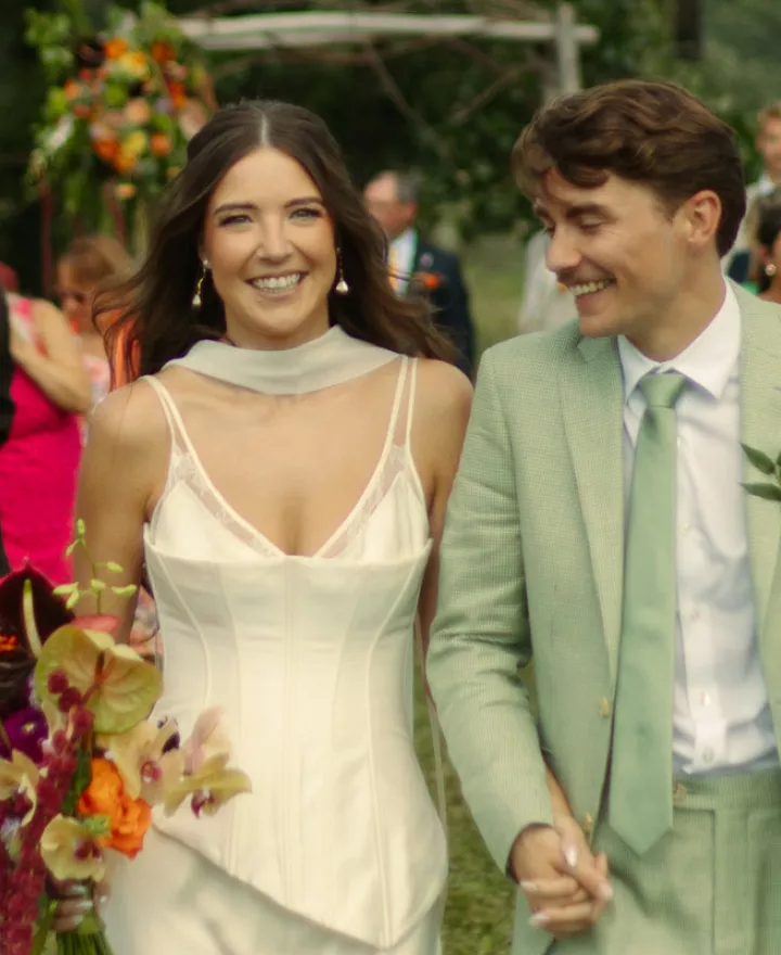 Sara and Billy smile and hold hands while they walk back down the aisle after their wedding ceremony