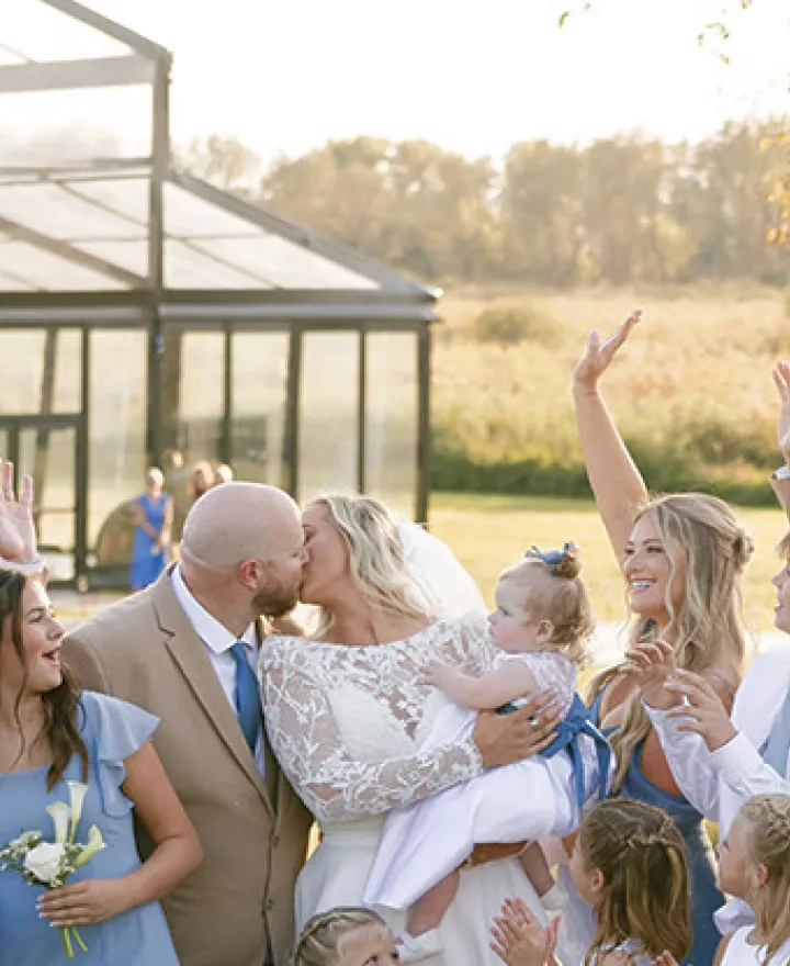 Monica and Matt kiss as their wedding party cheers on in celebration at private residence