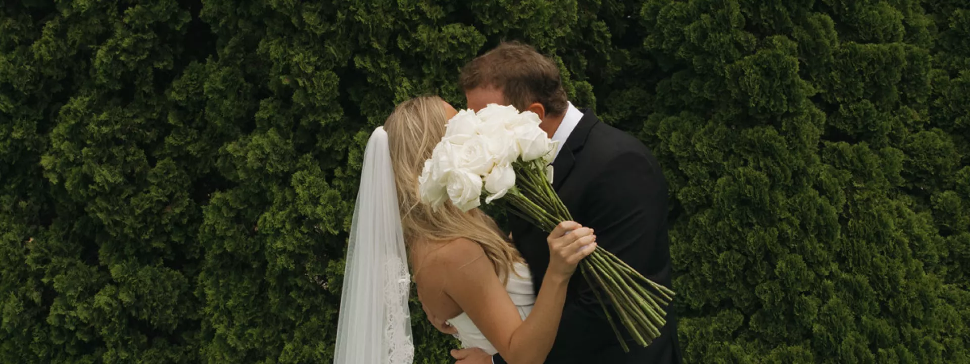 Sadie and Charlie share a kiss, hidden by a white rose bouquet