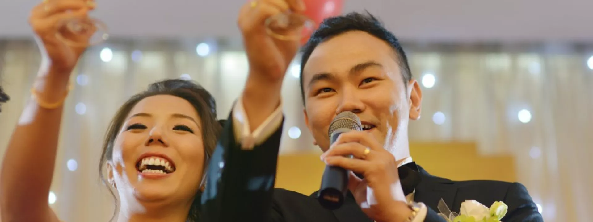 Smiling newlywed couple delivering a wedding reception toast with champagne and microphone, celebrating with heartfelt speeches and joyful energy