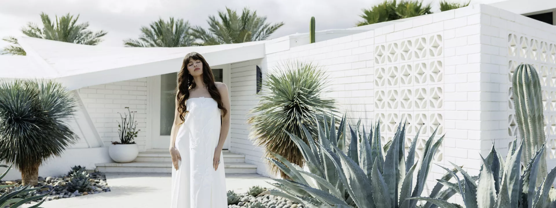Model poses in front of Desert White House in strapless wedding dress with subtle floral details