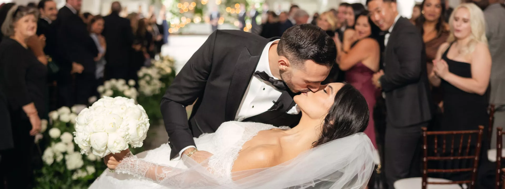 A gorgeous couple in classic wedding attire with long veil at elegant greenery altar with Armenian touches