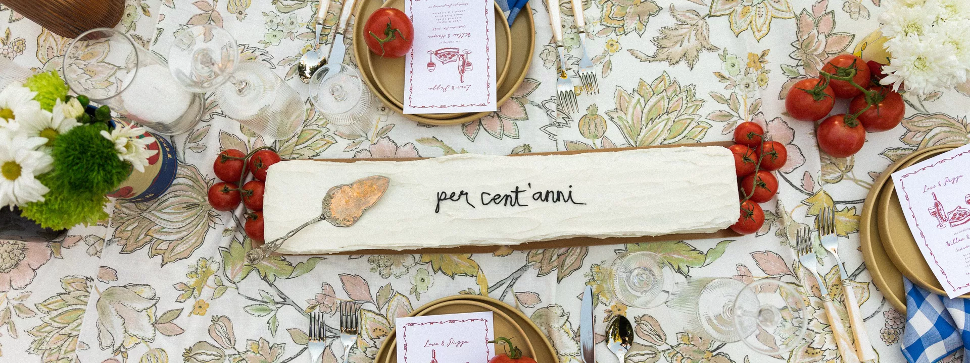 Horizontal cake with "per cent'anni" written in frosting on Italian-inspired tablescape featuring tomatoes as décor
