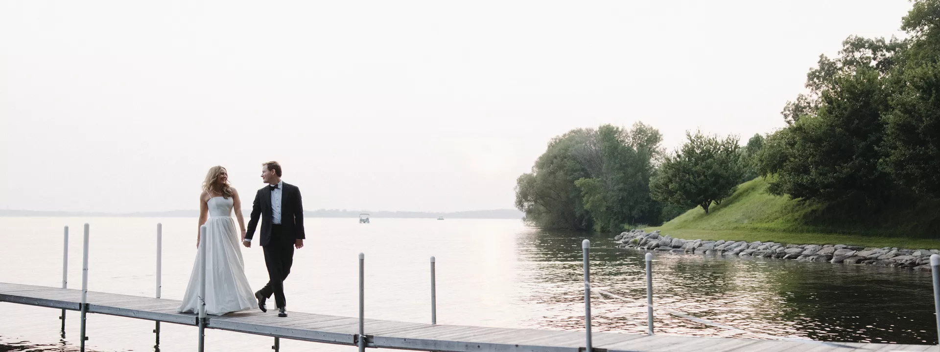 Abby and Jack walk on a dock on their lakeside wedding day at a private residence