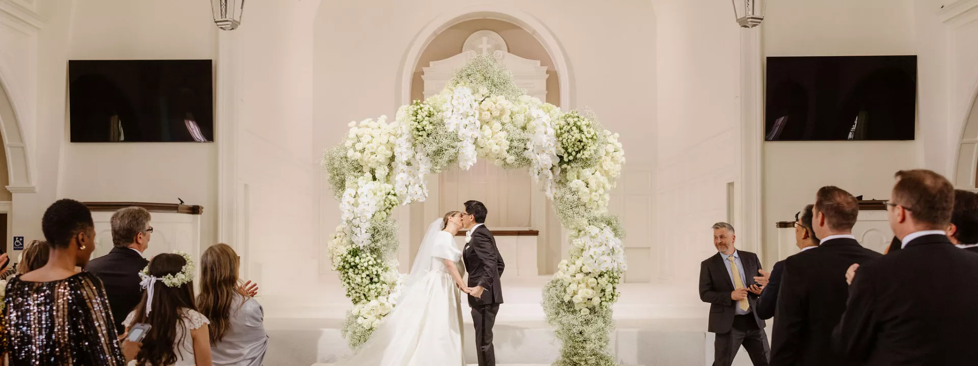 NBC Southern California newscaster Ted Chen shares a first kiss with his bride, Ariell Kirylo, under a breathtaking white floral arch at Vintage Church in Los Angeles.