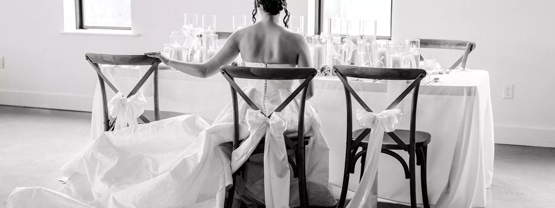 Bow Details Featured on Table Scape in Styled Shoot Black and white photo of a model wearing a bridal gown sitting at a table with bow detail