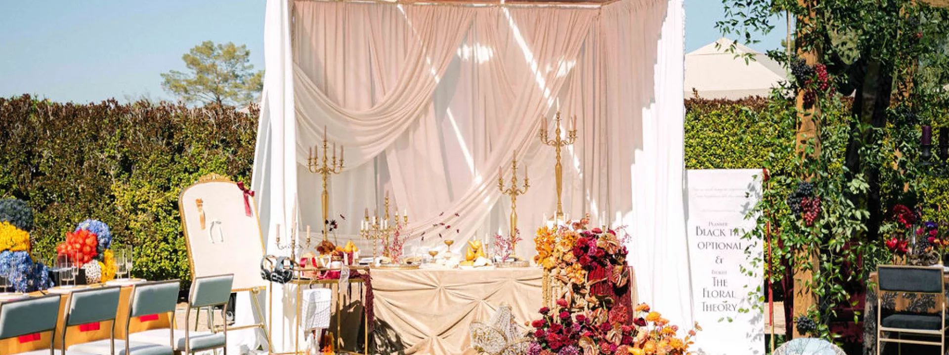 Elegant wedding table setup with draped fabric, gold candelabras, lush floral arrangements, and an interactive station featuring headphones and a writing station with ribbons.