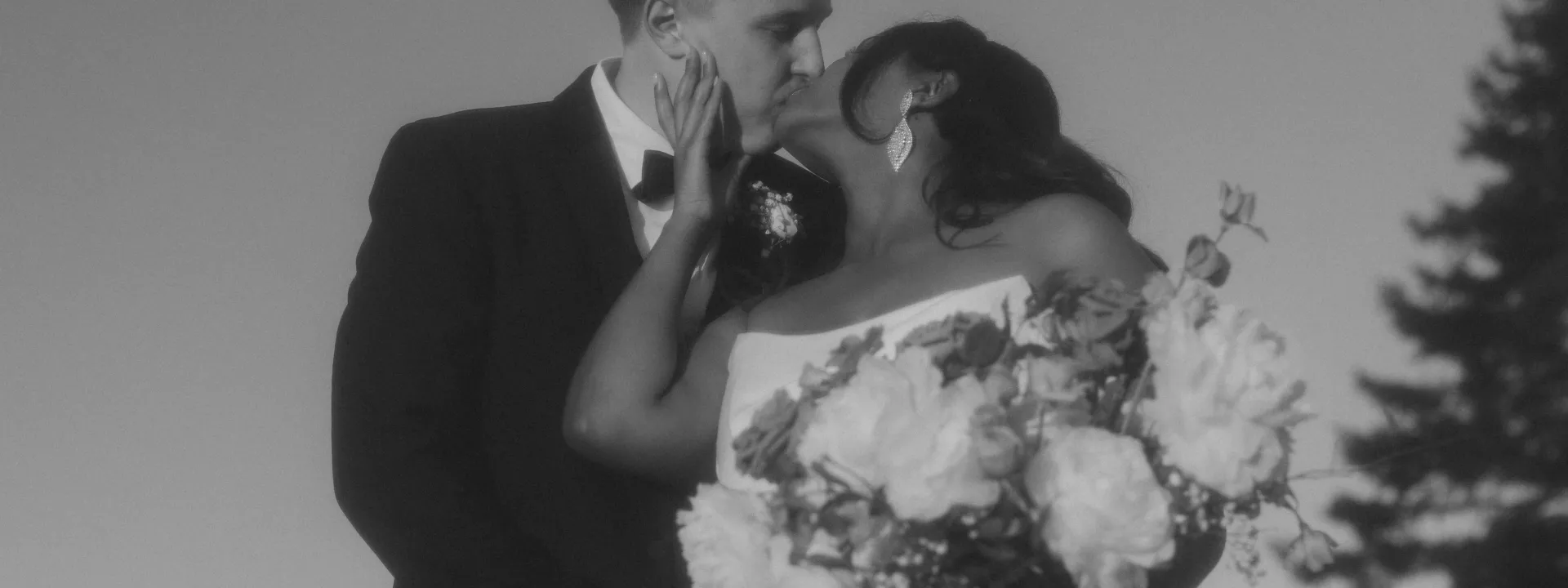 Tsion and Ben kiss in their wedding attire while showing Tsion's bouquet or peonies. 