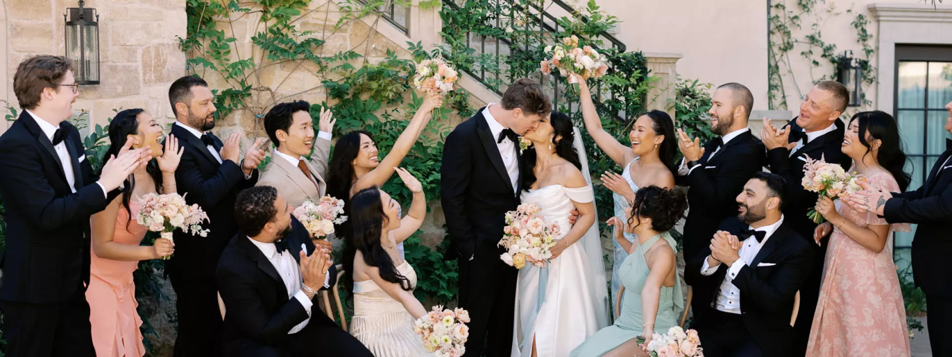 Bride and groom share a kiss while their wedding party cheers them on