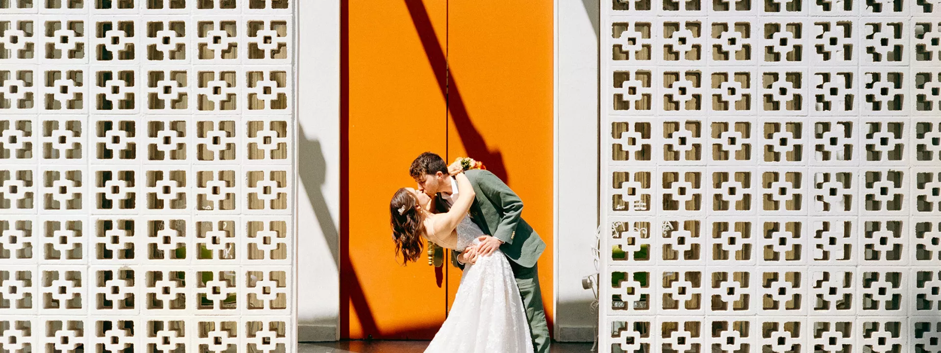 Bride and groom share a kiss against orange door in wedding day at Parker Palm Springs 