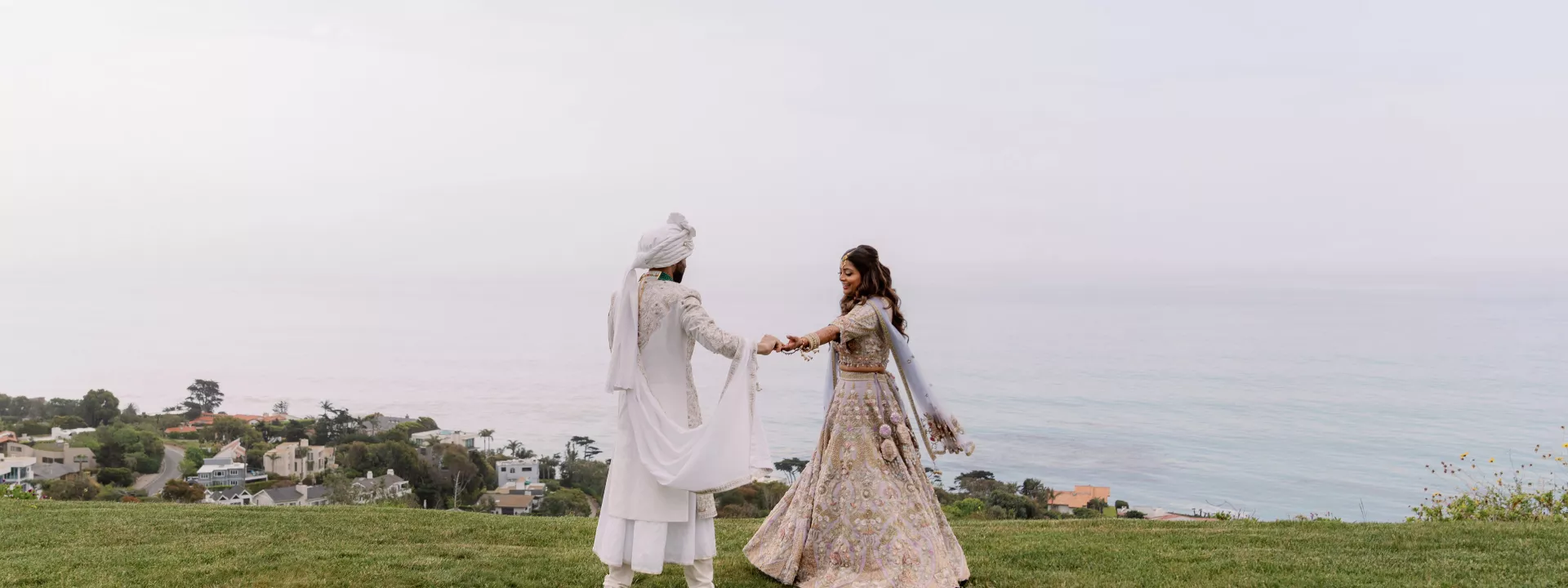 Bride and groom stand hand in hand with the misty coastline in the background