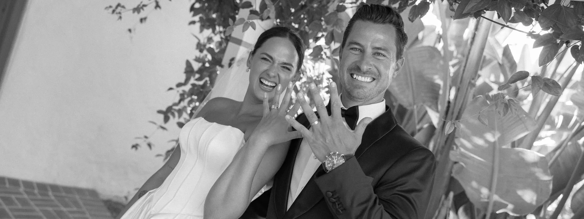 Bride and groom smile with their hands raise to show off their rings and newlywed status