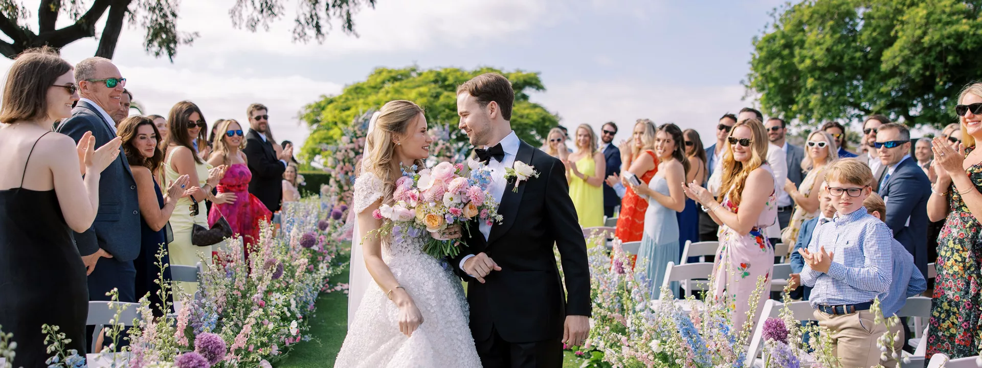 Bride and groom walk back down outdoor floral lined aisle after getting married at La Jolla Country Club