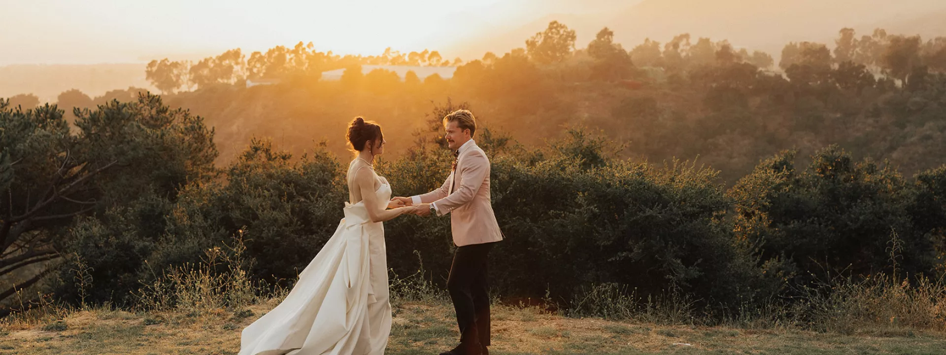 Bride and groom stand in golden hour glow against scenic vista 