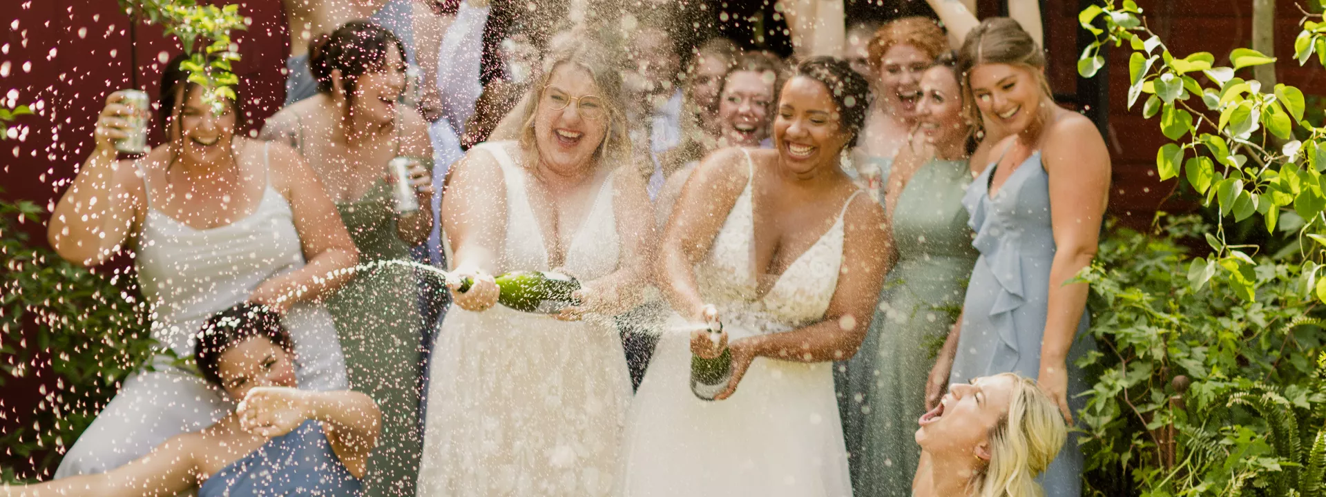 Brides spray champagne bottle surrounded by their bridal party