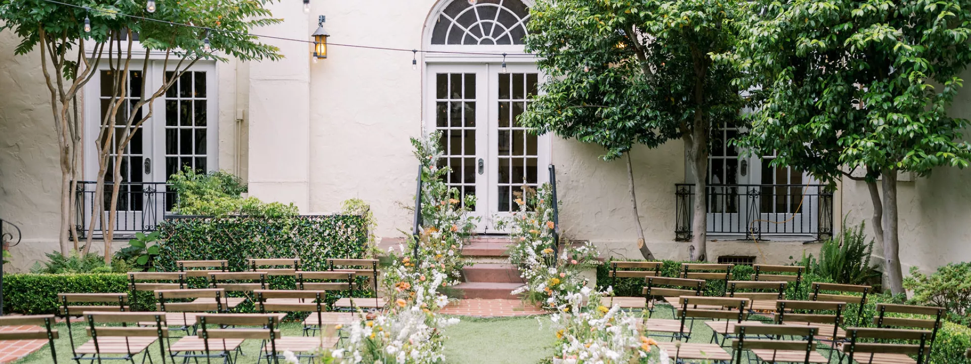 Wedding aisle and chairs and florals in front of a large window and tree