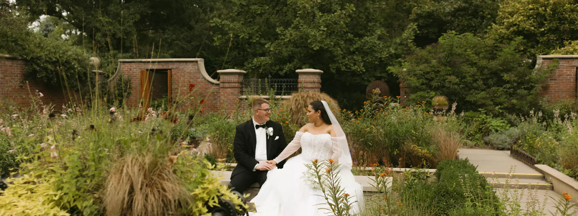 Gali and trevor sit on a bench in their wedding attire