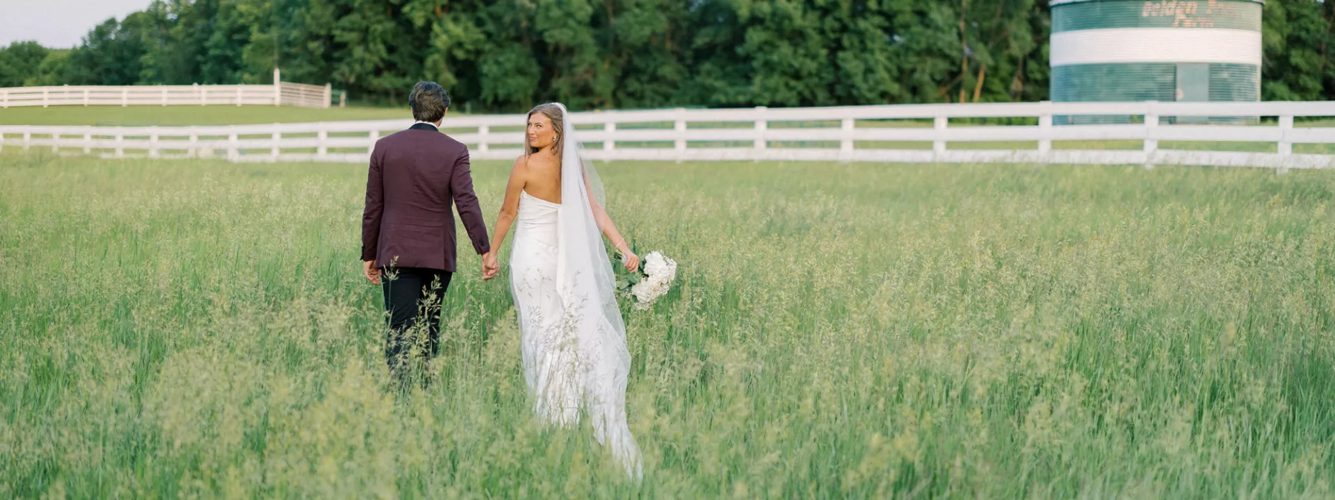 Bride and groom hold hands walking through the field of a private estate