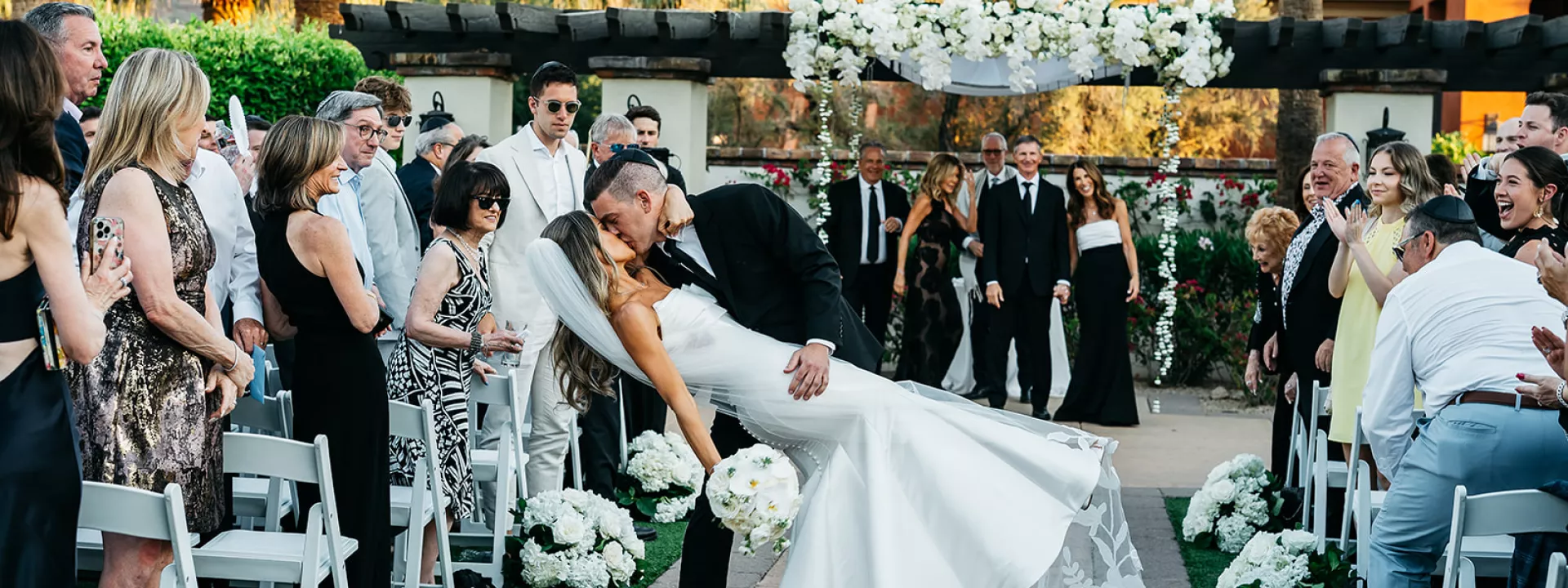 Groom dips bride into kiss at the end of floral-lined aisle at The Omni Scottsdale Montelucia