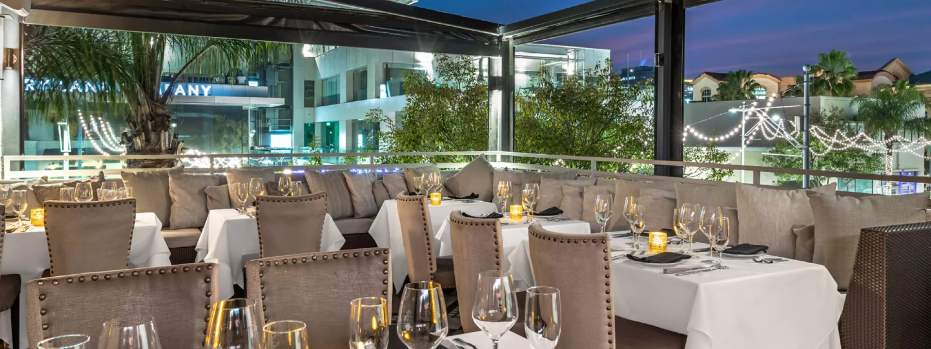 Rooftop dining terrace at Mastro’s Beverly Hills set for an evening event with white linens, candlelight and plush seating under a retractable roof.