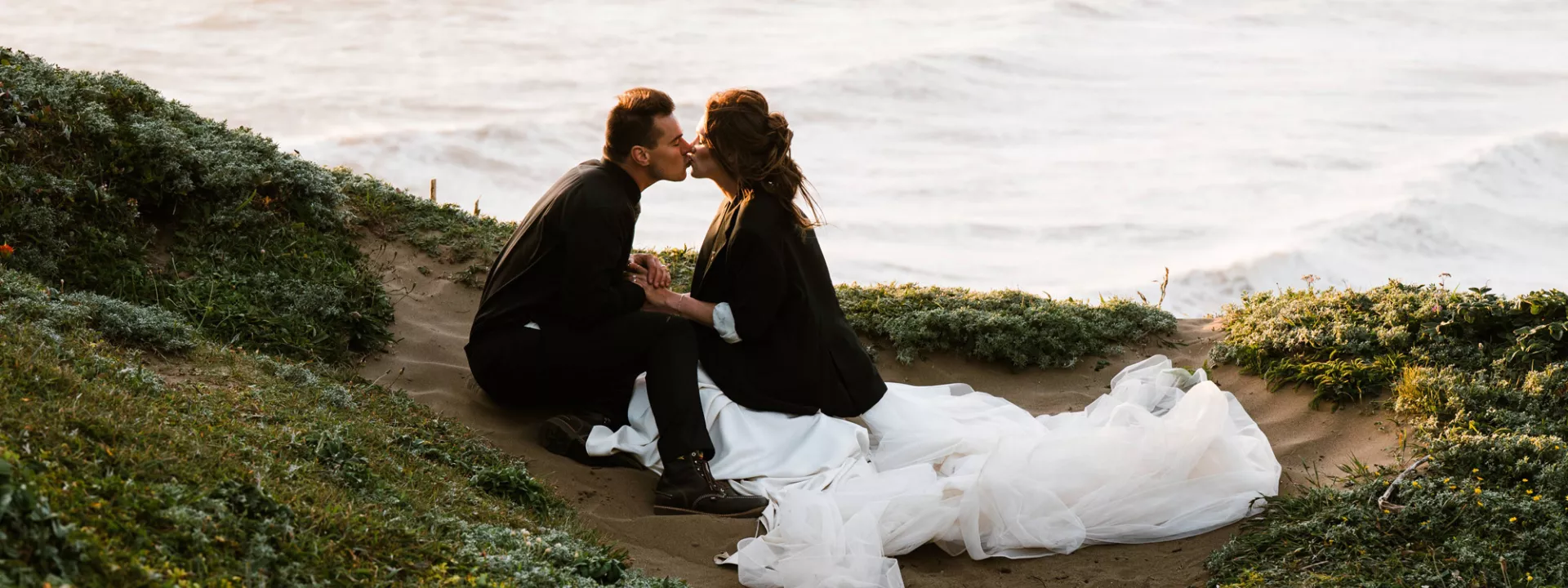 Olivia and Brian sit and share a kiss during their wedding day portraits on the southern coast of Oregon