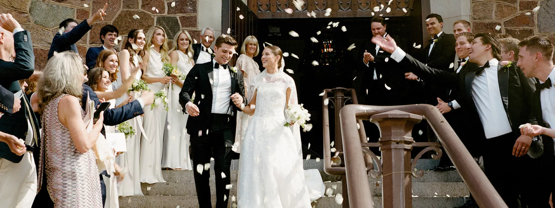 Isabel and John descend the staircase after ceremony t Plymouth Congregational Church as petals waft through the air