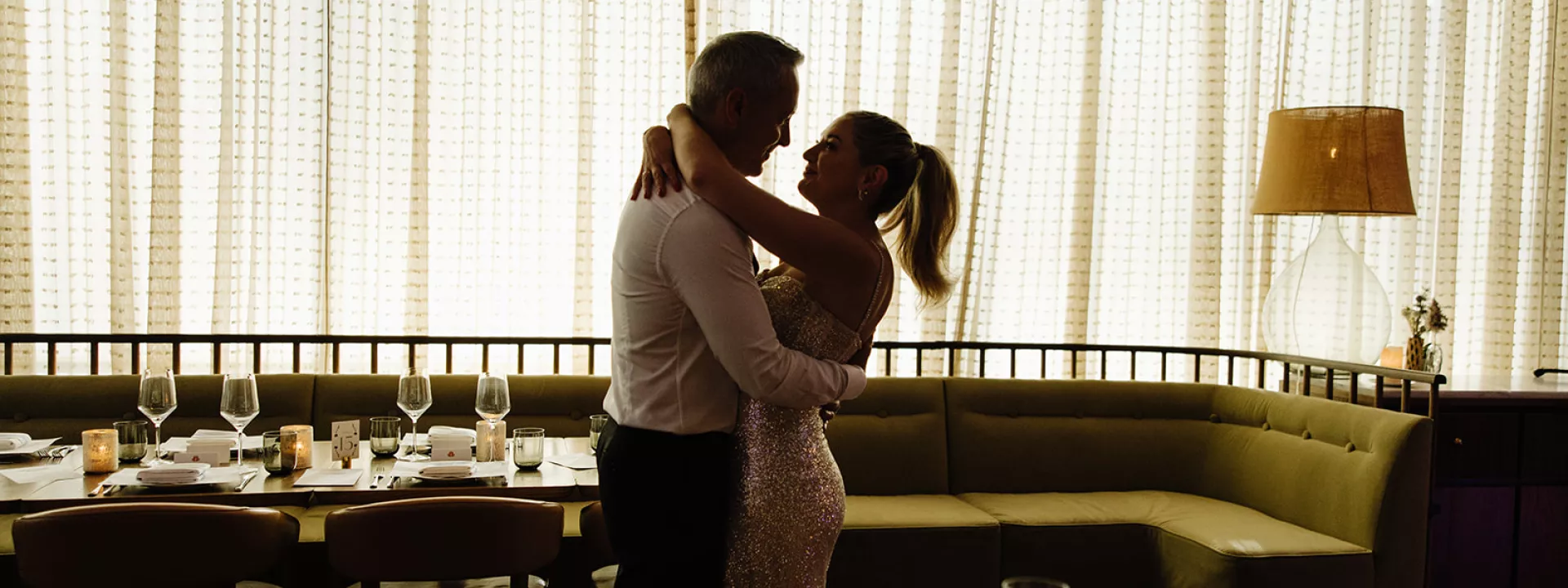 Kate and Tim embrace amidst reception scene at Mara