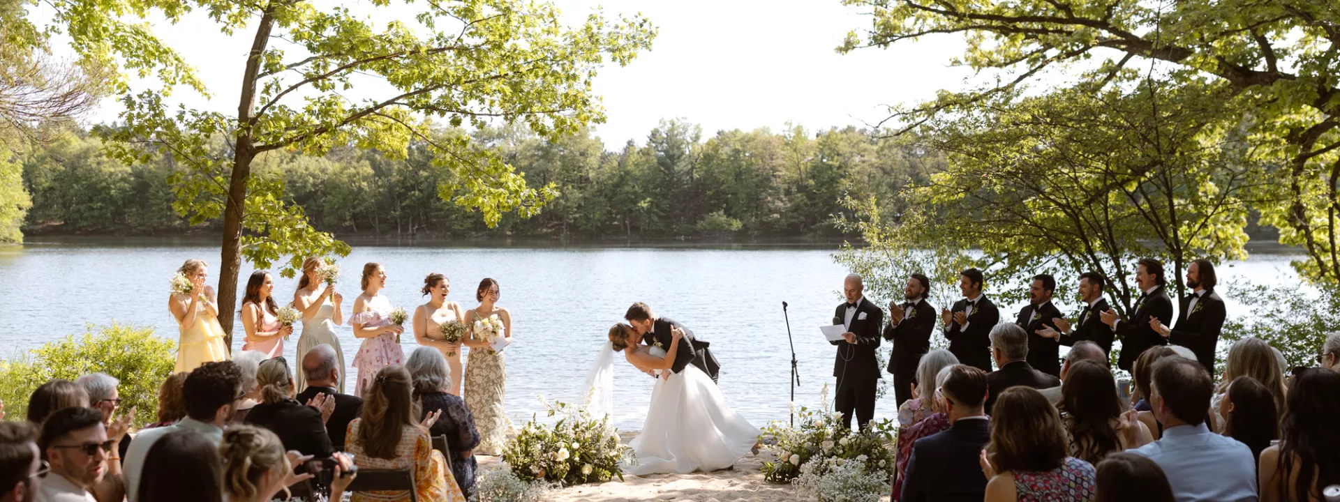 Molly and Ralph kiss at the altar in their outdoor ceremony framed by trees and their loved ones at Camp Elsewhere