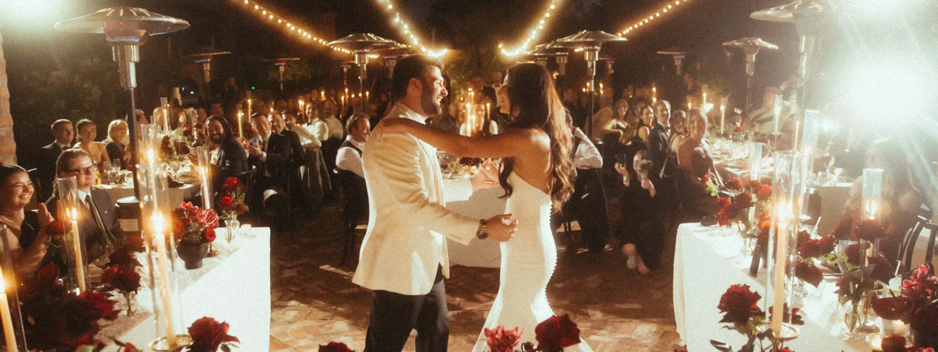 Bride and groom share a dance framed by their candlelit outdoor reception featuring bold red flowers at Royal Palms Resort and Spa