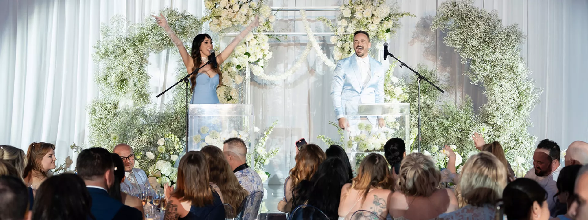 Weddings Royale emcees present on stage in front of a white floral arch and cheering audience at the California Wedding Day Best of 2025 awards ceremony