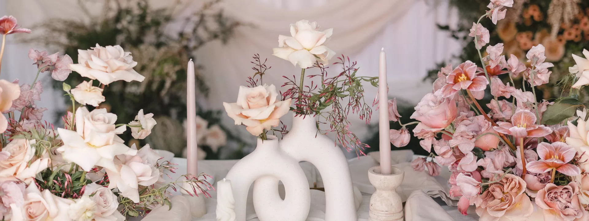 Tablescape featuring rosy hues and sculptural stone vases in imagined reception