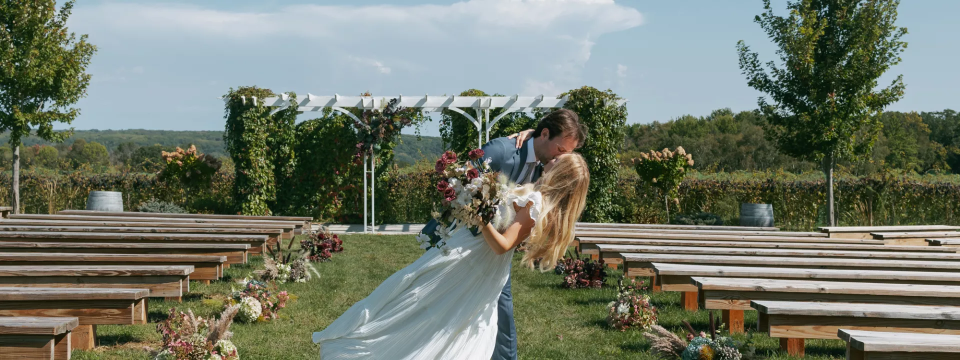 Groom dips bride and they share a kiss at the end of the aisle on the grounds of Rustic Roots Winery