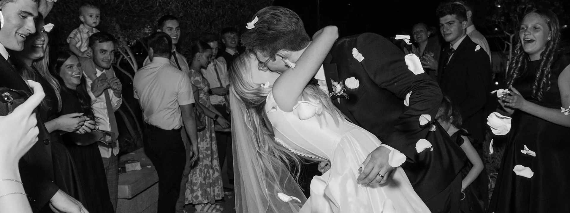 Bride and groom share a celebratory kiss while rose petals rain over them in wedding day at a family farm