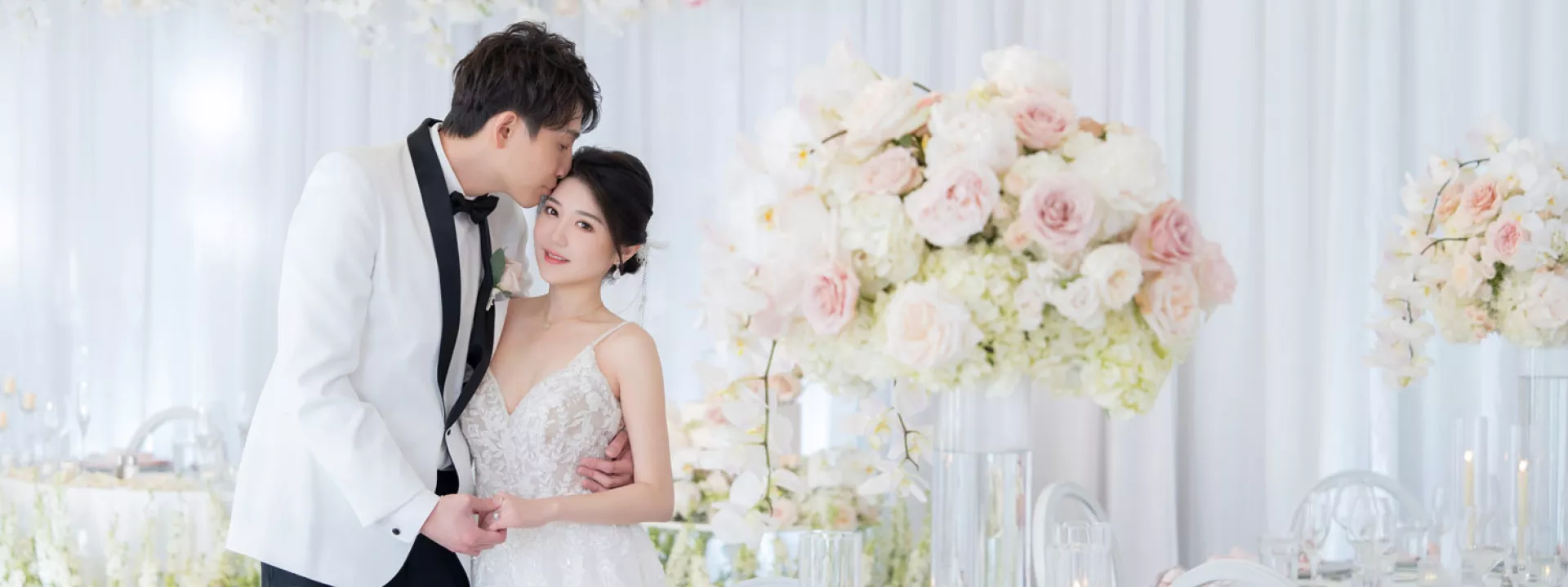 Bride and groom share a romantic moment at their reception, surrounded by soft white and blush floral arrangements at their oceanfront wedding at Hyatt Regency Huntington Beach