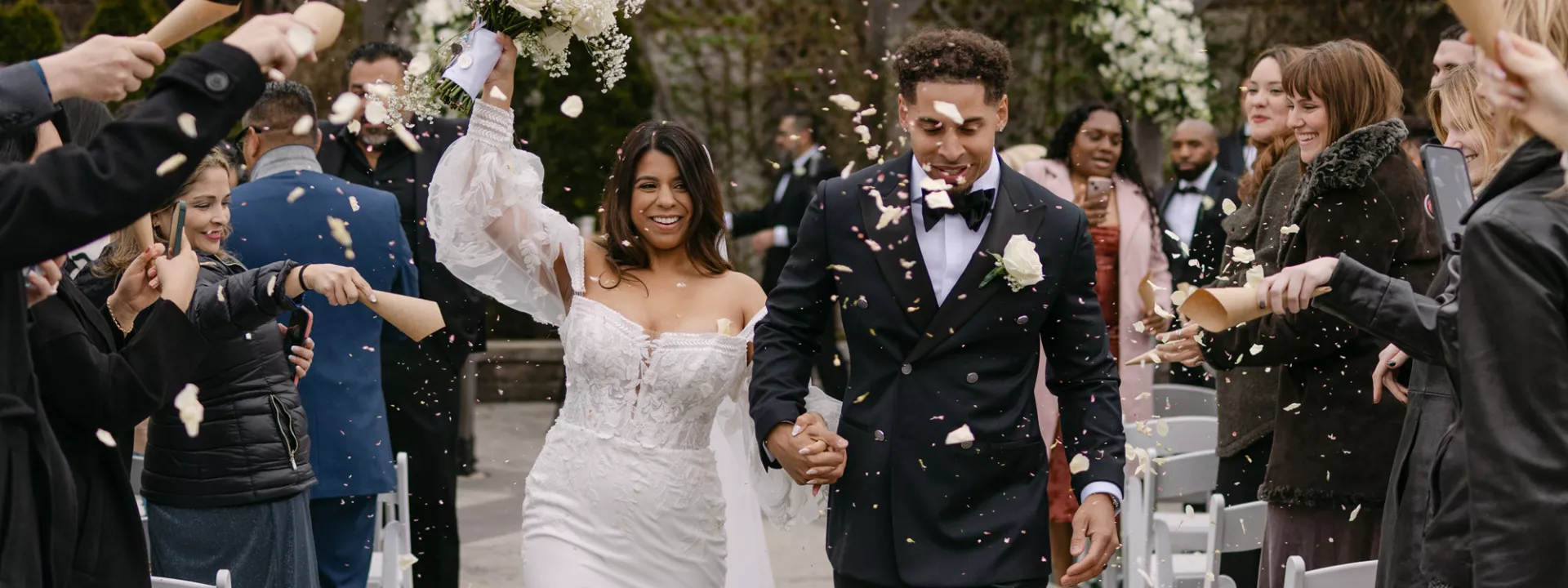 Bride and groom walk back down the aisle after exchanging vows, celebratory petals raining over them at The Ivy House