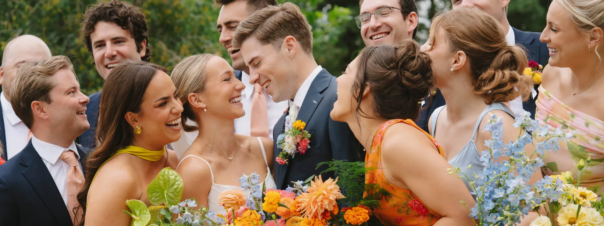 Wedding party surrounds the bride and groom as they share a loving glance