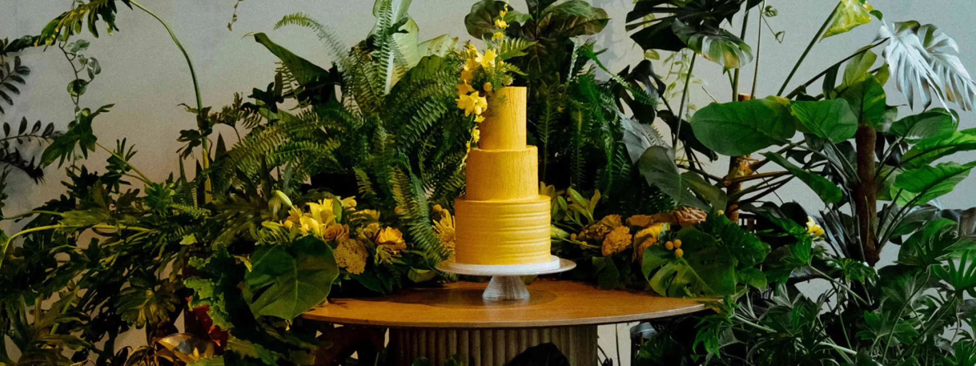 Bold, mango-hued tiered cake surrounded by lush verdure in imagined wedding day 