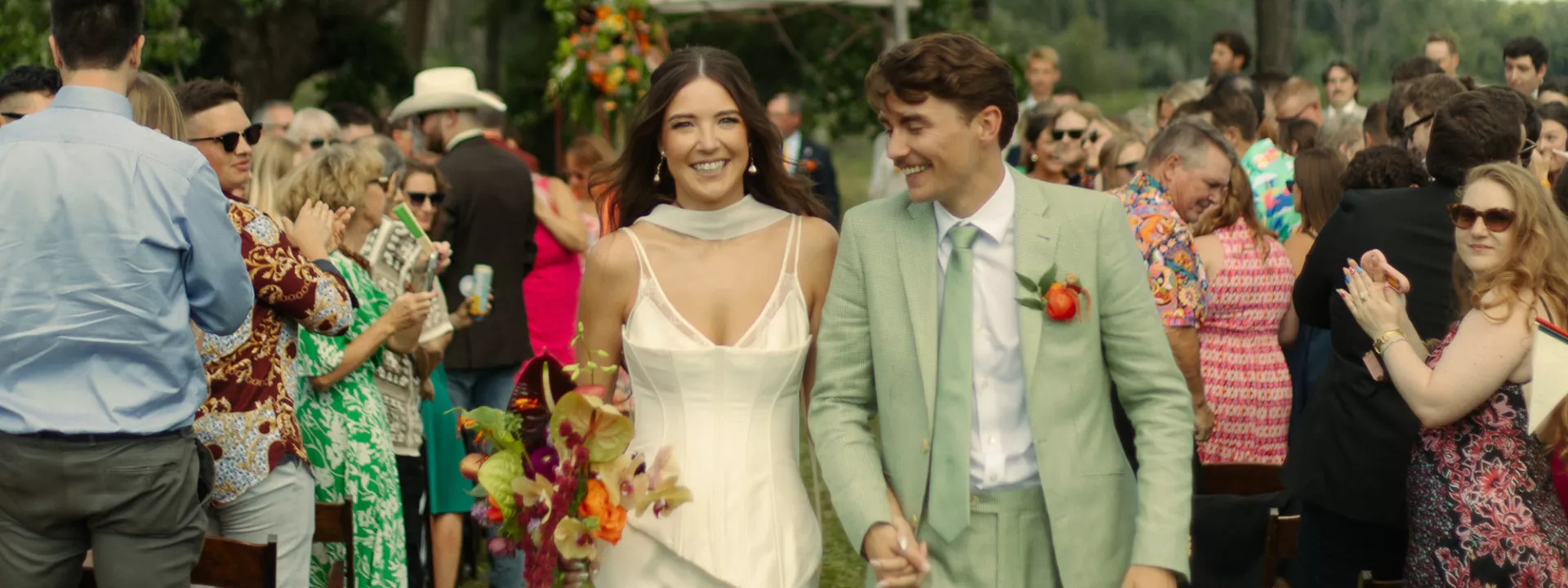 Sara and Billy smile and hold hands while they walk back down the aisle after their wedding ceremony