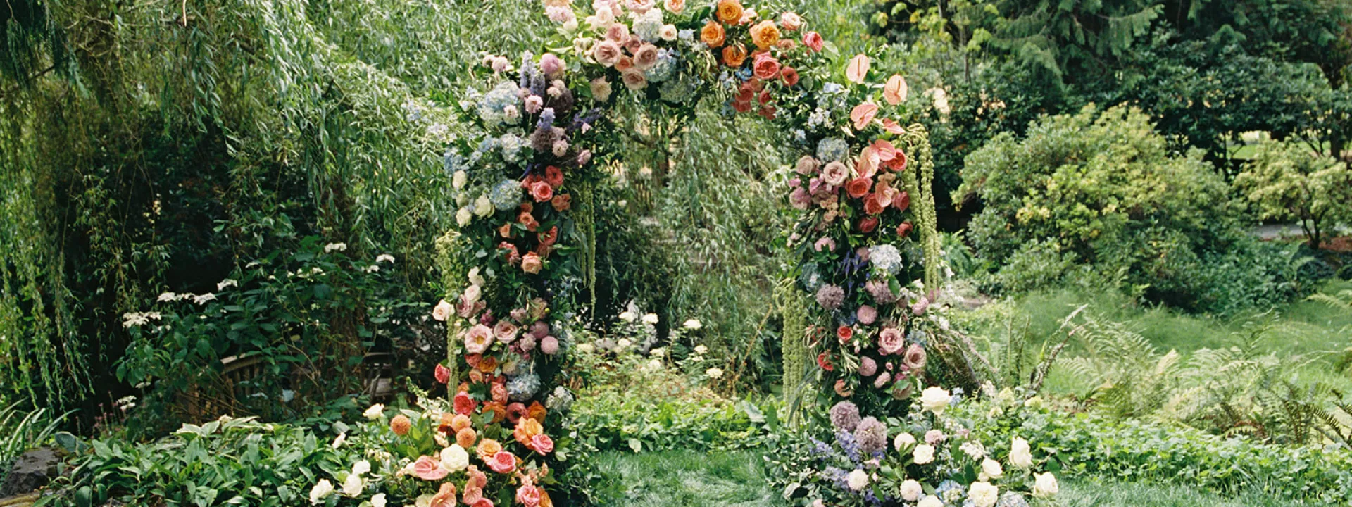 Lush floral arch against willow trees on grounds of Chateau Lill