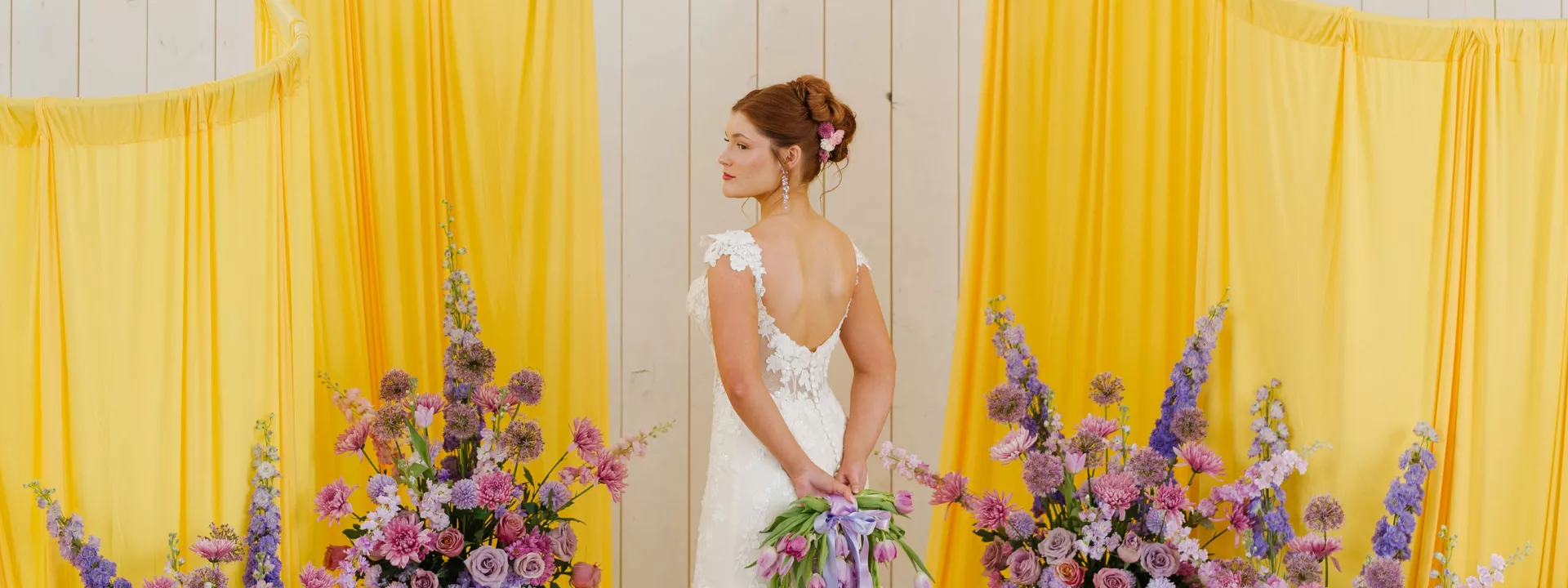 Model poses at altar with yellow fabric structures and lavender florals 