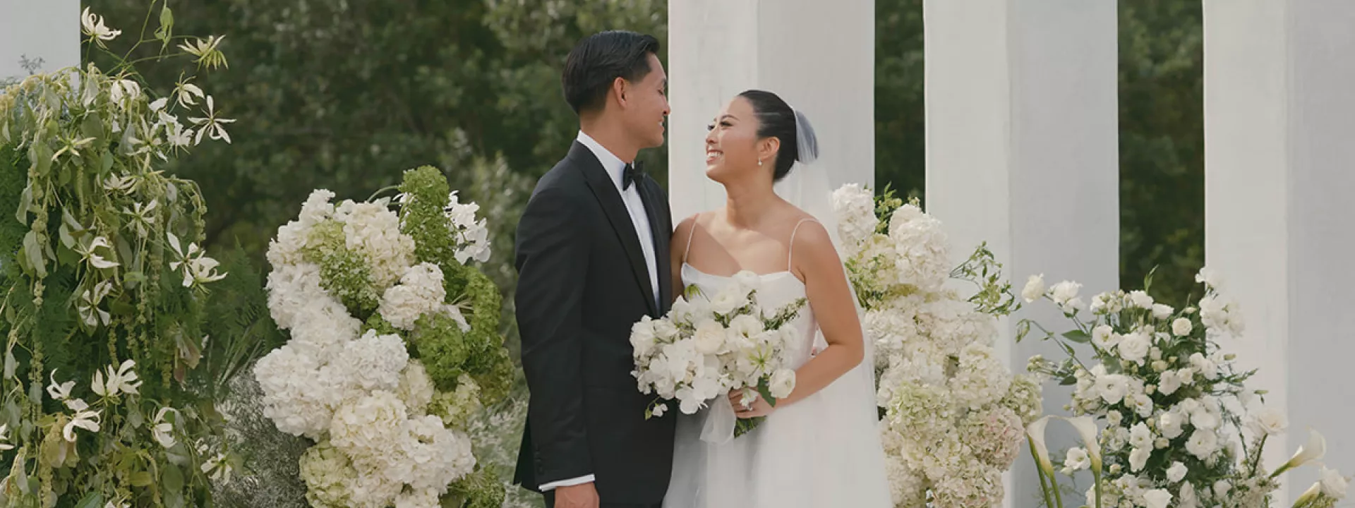 Bride and Groom smile at each other in front of modern altar surrounded by lush organic florals