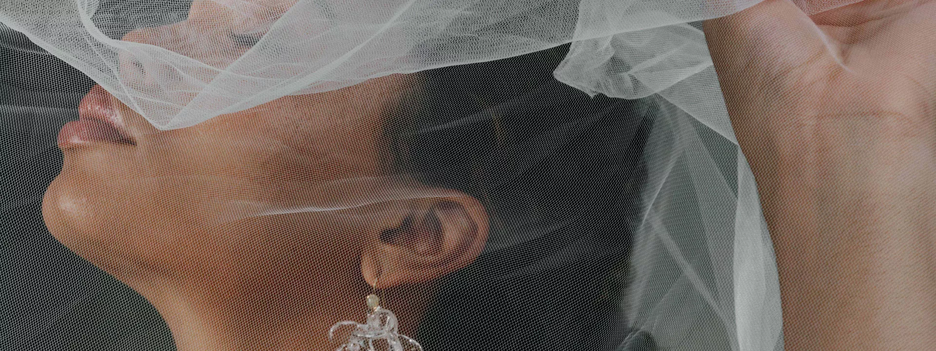 Model poses with holding veil over her face, showcasing stunning accessories in editorial shoot