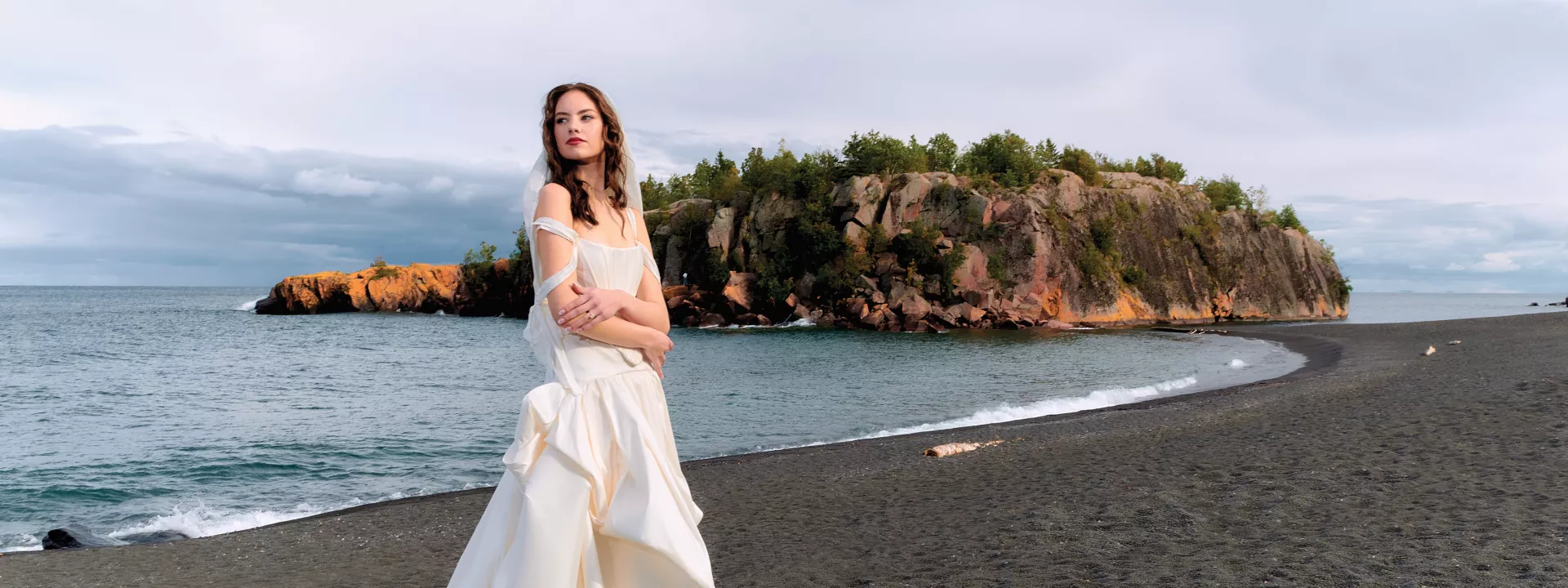 Model poses in fashion-forward wedding gown on the Black Sand Beach with Lake Superior in the background