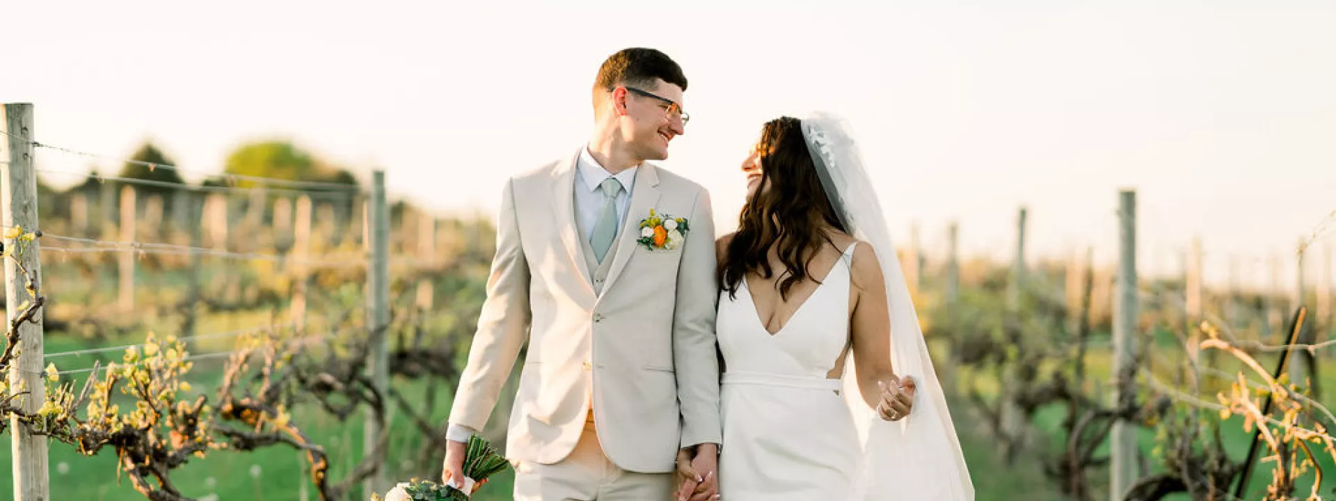 Bride and groom smile at each other while walking through the grounds of Bella Terre Vineyard during golden hour