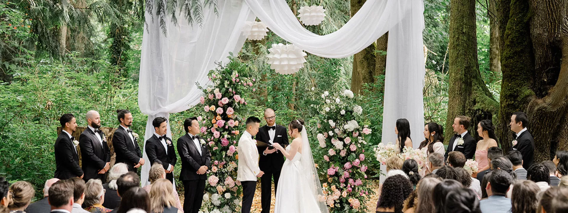 Bride and groom stand at draped outdoor altar for their ceremony, surrounded by their bridal party  at Twin Willow Gardens