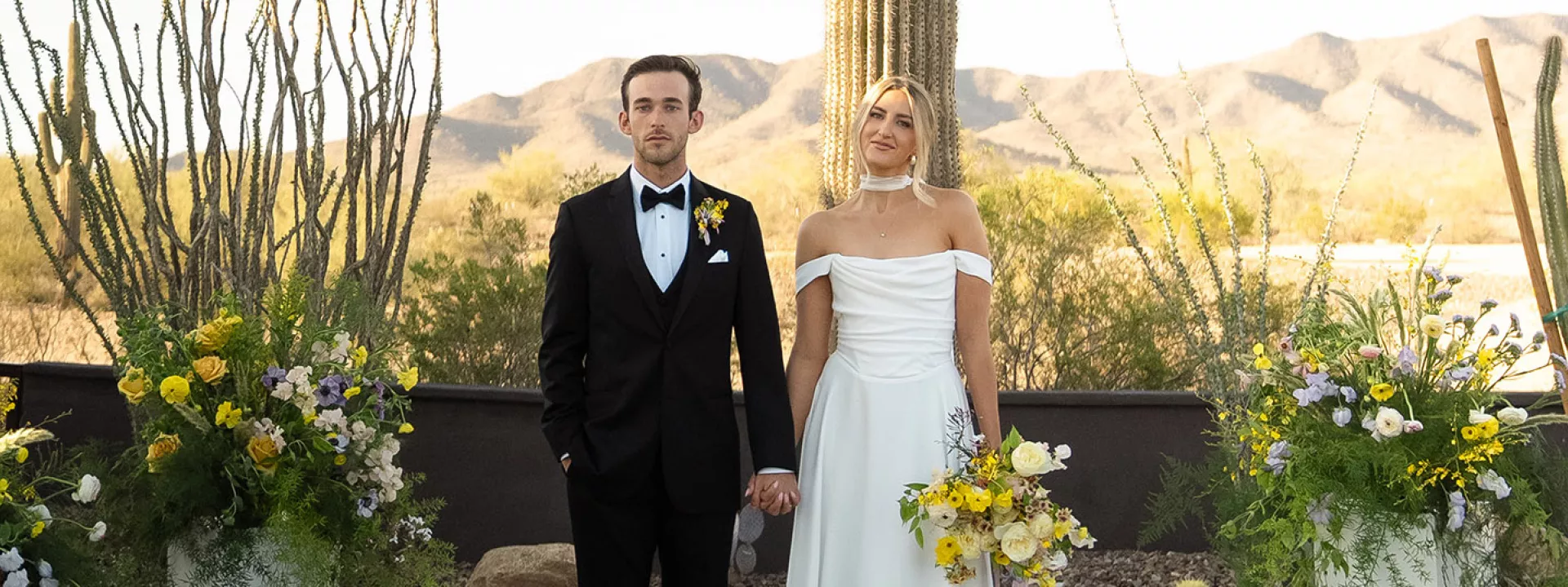 Bride and groom stand hand in hand at the altar, framed by bright blooms and cacti at The Willow Weddings & Event Center