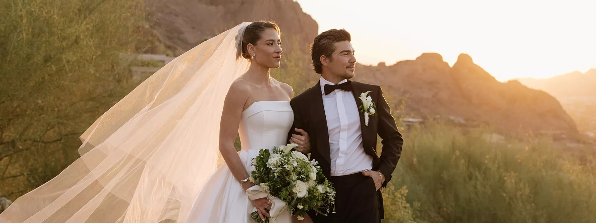 Bride and groom pose on the rocks of Camelback Mountain with the golden hour casting a glow behind them