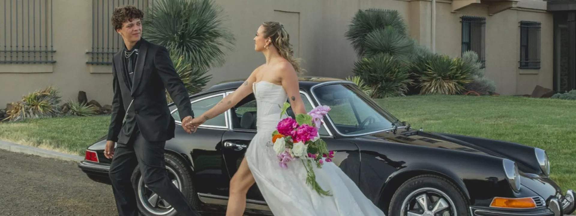 Groom leads bride across grounds of Maryhil Museum, a vintage car in the background